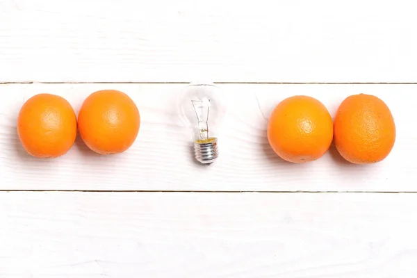 Electric light bulb and oranges in line on white background — Stock Photo, Image
