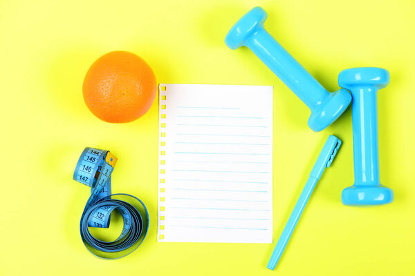 Ноутбук страница и оранжевые фрукты рядом с синей ручкой и гантели
