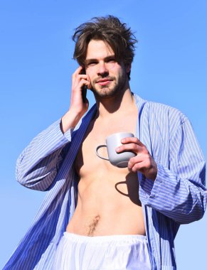 Mavi çizgili pijamalı, elinde fincanla beyaz maço.