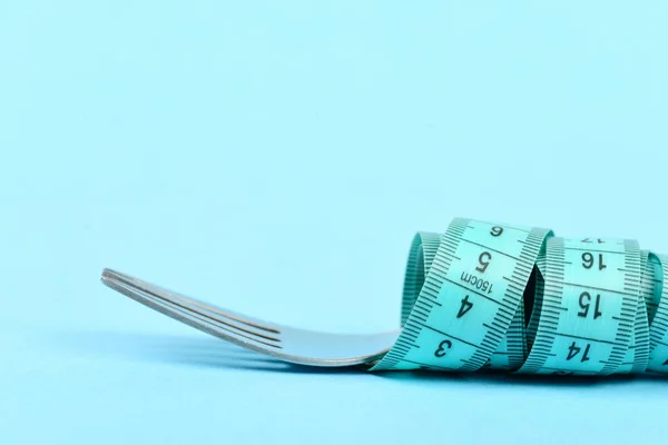 Fork and measuring tape tied around it, isolated on turquoise — Stock Photo, Image