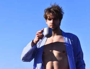 Mavi çizgili pijamalı, elinde fincanla beyaz maço.