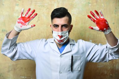 Kanlı elleri havada, ameliyat maskeli doktor.