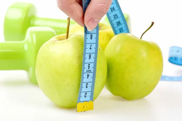 Apples measured by cyan flexible ruler in fingers, green dumbbells — Stock Photo, Image