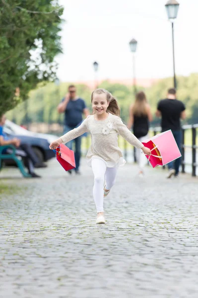 Hezká holčička běžící na ulici růžová nákupní tašky — Stock fotografie