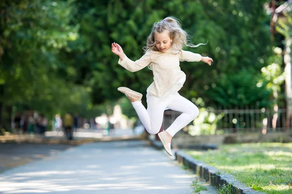 Söt liten tjej med lockigt blont hår hoppning på gatan — Stockfoto