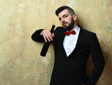 Süitte şık sakallı bir adam bir şişe şarap tutuyor.