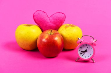 Çalar saat yanında üç elma ve pembe kalp