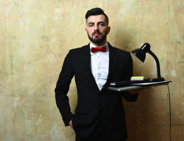 Sakallı ofis çalışanı dizüstü bilgisayar, lamba ve kırtasiye malzemesi tutuyor.