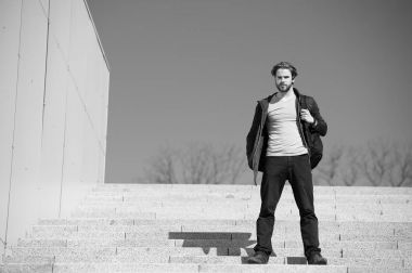 Mavi gökyüzü arkaplanına karşı basamaklarda oturan düşünceli genç adam