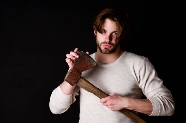 Sakallı ve dikkatli bakışlı adam yaşlı paslı baltayı tutuyor.