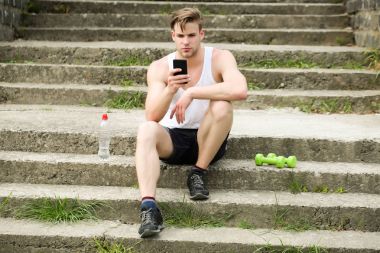 Ciddi yüzlü bir sporcu beton merdivenlerde telefonla oturuyor.
