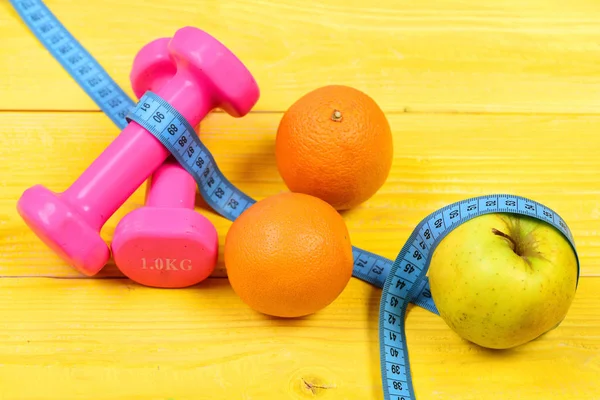 Sport and health concept, dumbbells weight with measuring tape, fruit — Stock Photo, Image