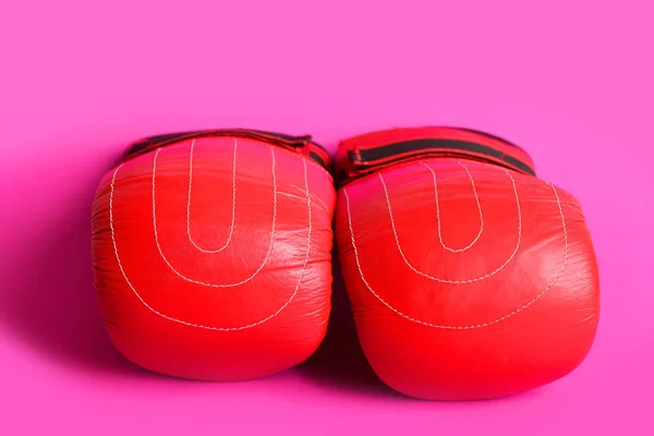 Bright red boxing gloves with white sewn stripes on pink