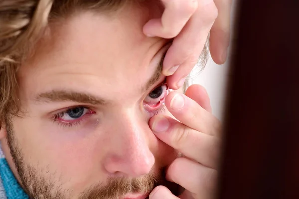 Человек с бородой и голубыми глазами надевает контактные линзы — стоковое фото