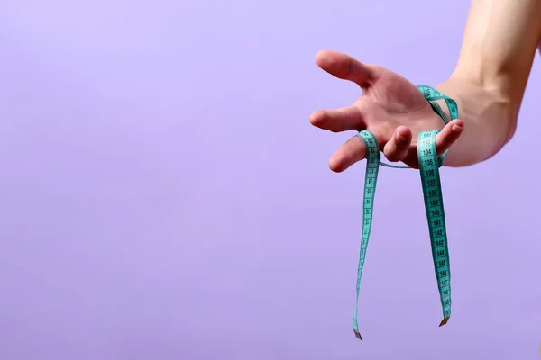 Hand van de mens met blauwe meetlint op paarse achtergrond — Stockfoto