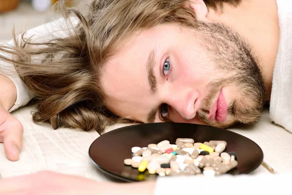 Pills on plate near motionless guy with beard
