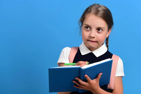 Pupil in school uniform with braid. Girl writes in notebook — Stock Photo, Image