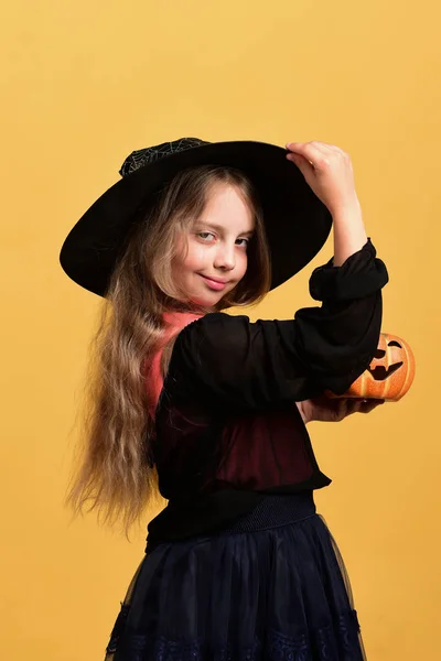 Chica con calabaza naranja tallada aislada sobre un fondo amarillo cálido —  Fotos de Stock