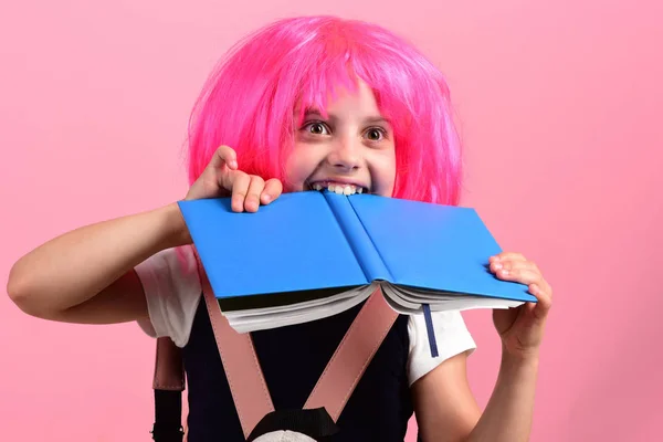 Pupil with pink wig. Girl bites big blue book.