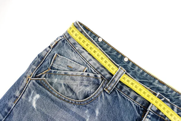 Conceito de dieta: jeans com fita métrica amarela em vez de cinto — Fotografia de Stock