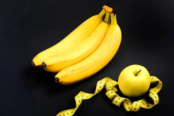 Бананы и раскрученная измерительная лента вокруг зеленого яблока — стоковое фото