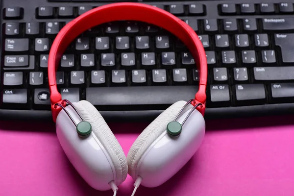 Electronic appliances on pink background. Headphones and black keyboard