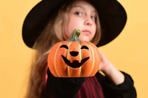 Kid in black witch hat and dress. Girl with pumpkin