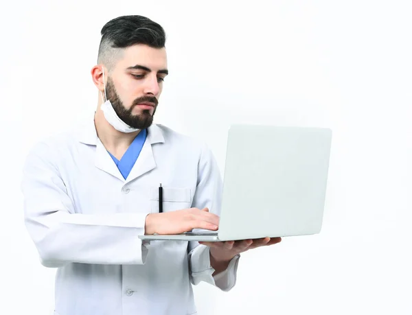 Arzt mit Bart benutzt weißen Laptop. Guy trägt chirurgische Maske — Stockfoto
