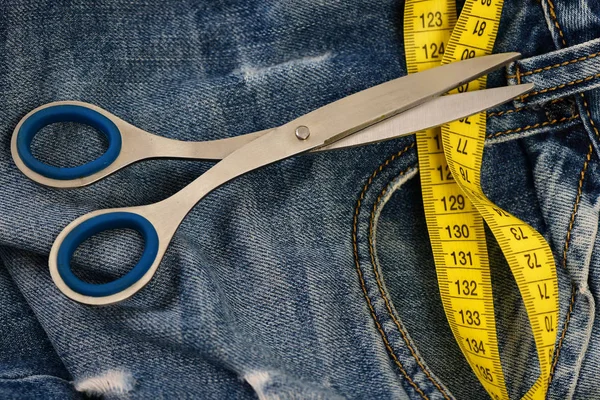 Ножницы и лента для измерения на джинсах как концепция одежды — стоковое фото