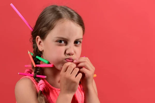 Kid in roze outfit met vlechten, gekleurde potloden en stiften — Stockfoto