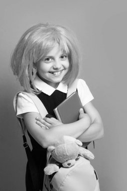 Sırt çantası, kitabı ve oyuncağı olan kız. Pembe peruklu kız öğrenci.