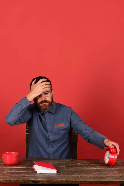 Muž s plnovousem a brýlemi drží budík, červené pozadí — Stock fotografie