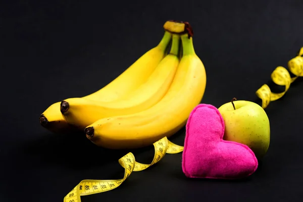 Bananas and apple near pink heart and tape measure — Stock Photo, Image