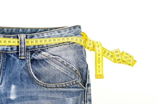 Conceito de dieta: Calça jeans azul com fita métrica amarela em torno da cintura — Fotografia de Stock