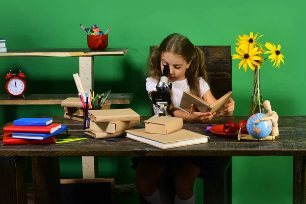 Школьница с концентрированным лицом держит книгу. Девушка смотрит в микроскоп — стоковое фото