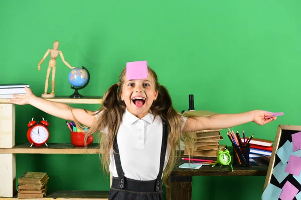 Schoolmeisje met vrolijk gezicht en roze notitie op voorhoofd — Stockfoto