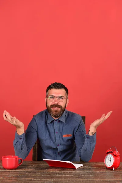 Вчитель з бородою і окулярами сидить біля блокнота, червоний фон — стокове фото