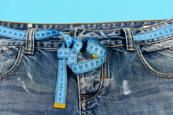 Jeans with blue measure tape around waist on blue background — Stock Photo, Image
