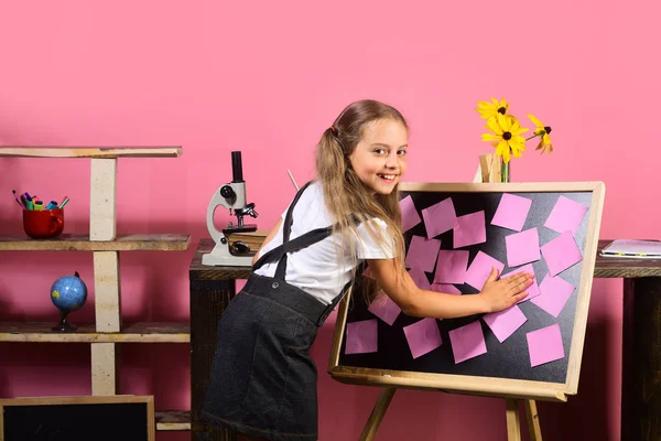 Menina coloca notas pegajosas rosa no quadro negro — Fotografia de Stock