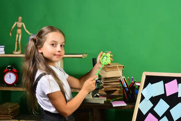 Menina mostra o tempo no relógio verde com seu lápis — Fotografia de Stock