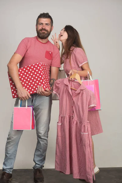 Casal segurando sacos de compras e roupas em fundo cinza — Fotografia de Stock