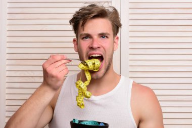 Kolsuz tişörtlü, dağınık saçlı ve mezura yiyen adam.