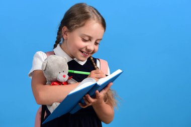 Kız oyuncak ayıyı tutuyor ve mavi defterine yazıyor.