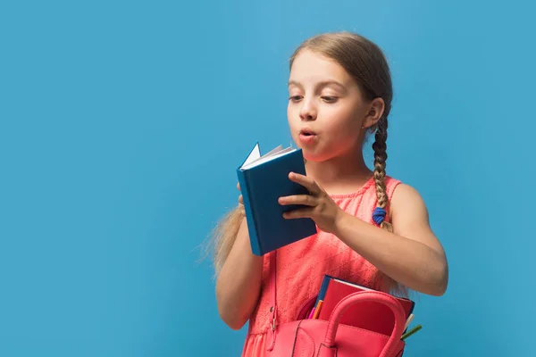 Chica con bolsa rosa apertura libro azul sobre fondo azul — Foto de Stock