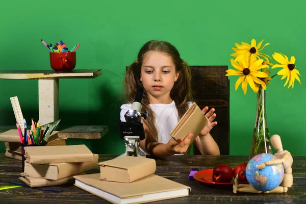 Estudante com rosto sério detém livro e olha para o microscópio — Fotografia de Stock