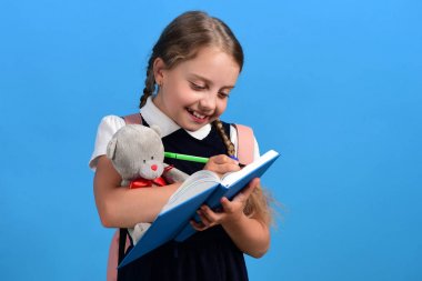 Kız mavi not defterinde yazıyor ve oyuncak ayı tutar