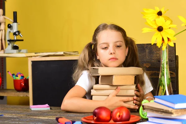 Девушка сидит за столом с грудой книг, цветов, фруктов — стоковое фото
