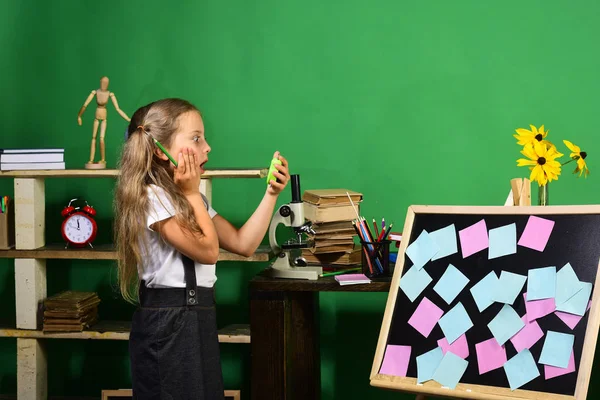 Menina segura relógio verde e lápis em pé por quadro-negro — Fotografia de Stock