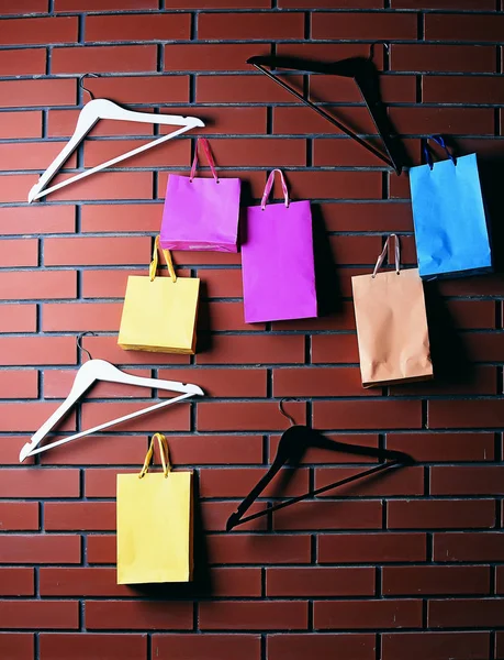 Färgglad shopping väska och garderob hängare på brun tegelvägg — Stockfoto