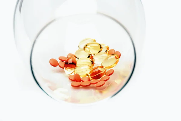 Pílulas vermelhas e cápsulas de óleo de fígado de bacalhau em vidro — Fotografia de Stock